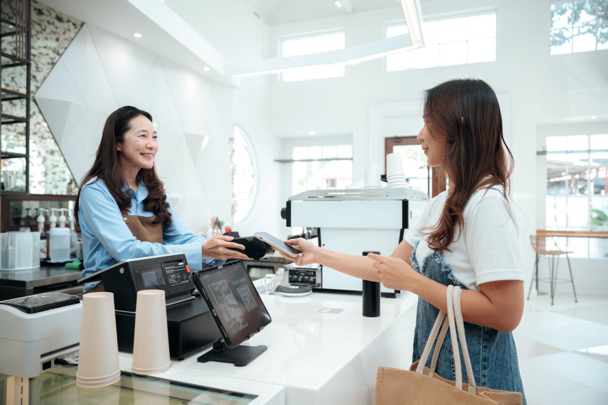 Cafe owner hands a tablet payment terminal to a customer at the counter.