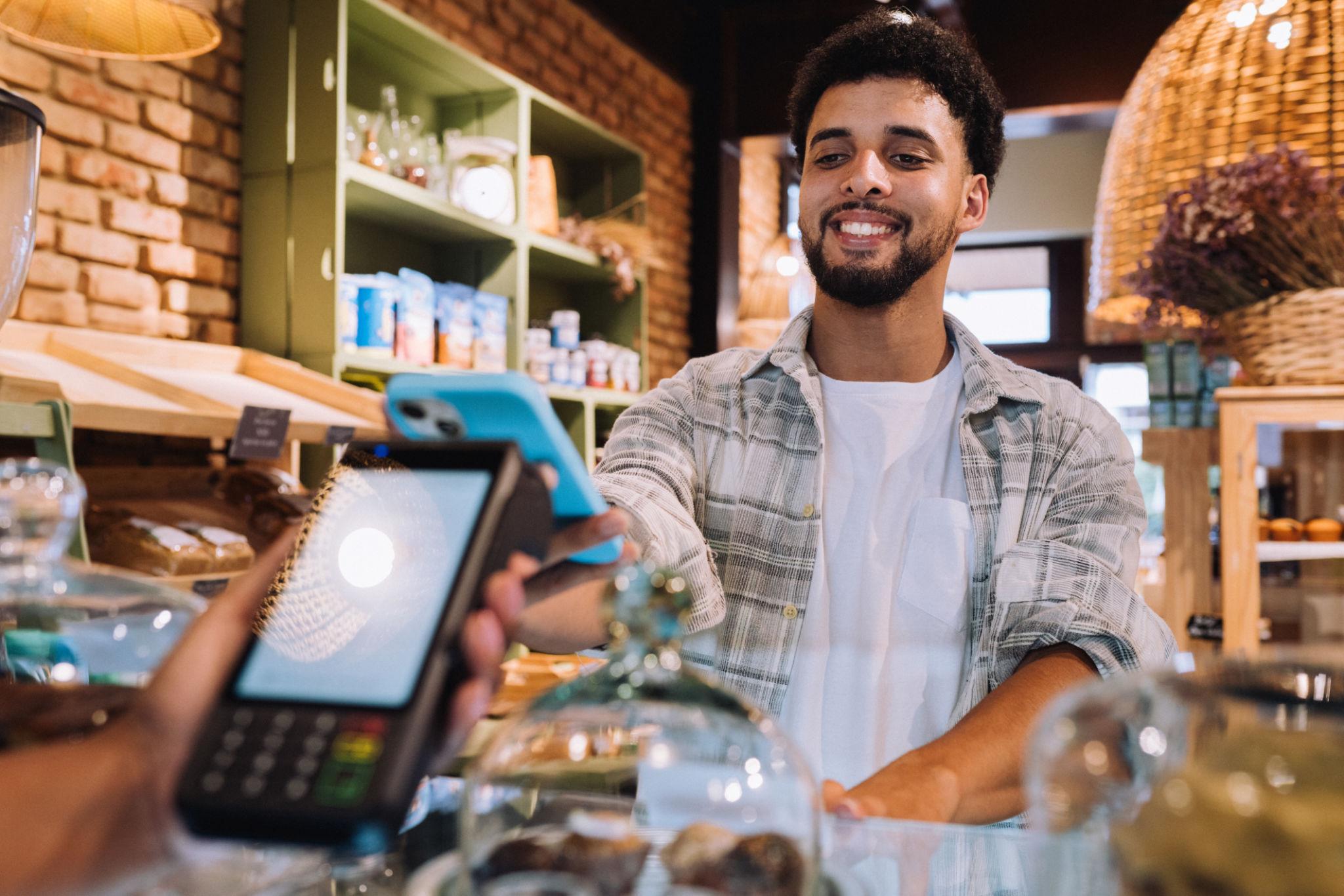 Bakery cashier accepting a phone tap at the payment terminal in a warm-lit shop.