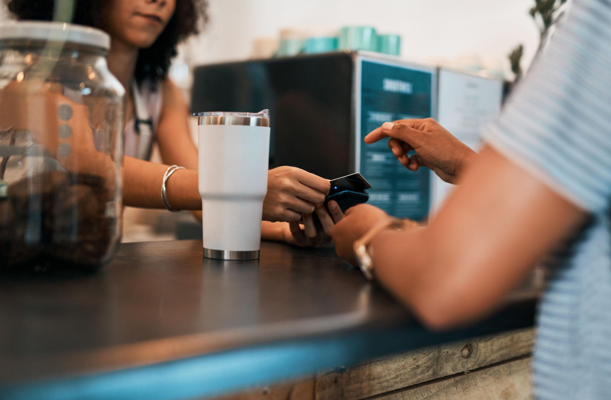 Close-up of two hands at a cafe counter completing an anonymous tap-and-go payment.